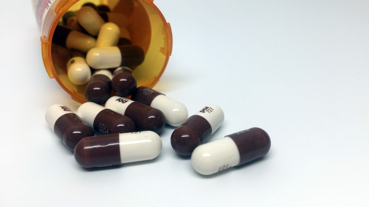 Yellow and white doxycycline capsules beside an open medication bottle.