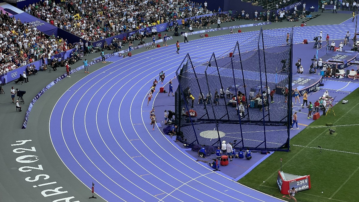 Runners from a heat of the mixed 4 by 400 metres relay strung out around the bend of the purple track at the Stade de France during the Paris 2024 Olympics, with a crowd in the stands and a Mixed 4x400 marker on the infield.