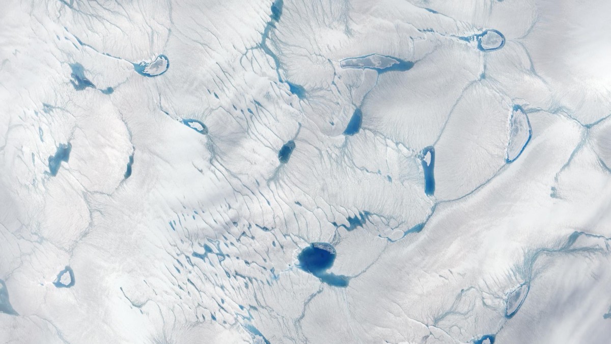 Satellite view of blue meltwater channels and ponds crossing Greenland's white ice sheet.