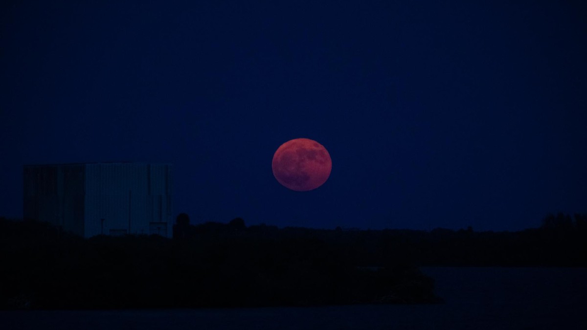 A bright full Moon rising in a dark blue evening sky above NASA's Kennedy Space Center.