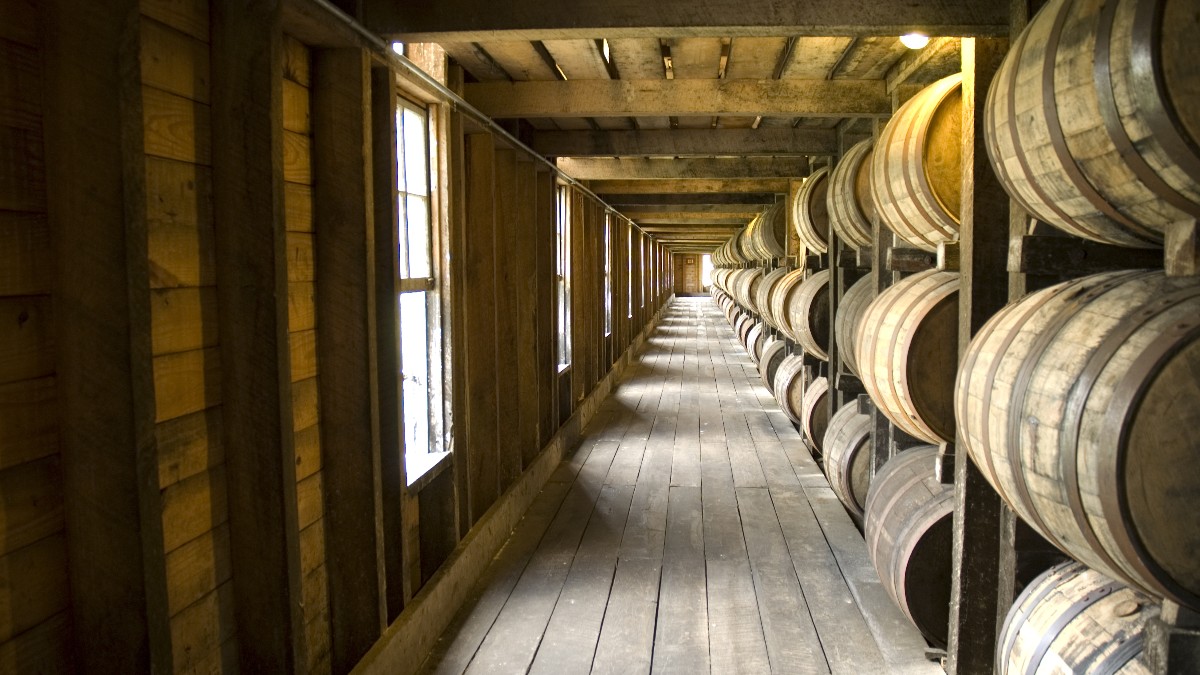Rows of whiskey barrels stacked along a long room in a bourbon distillery warehouse.