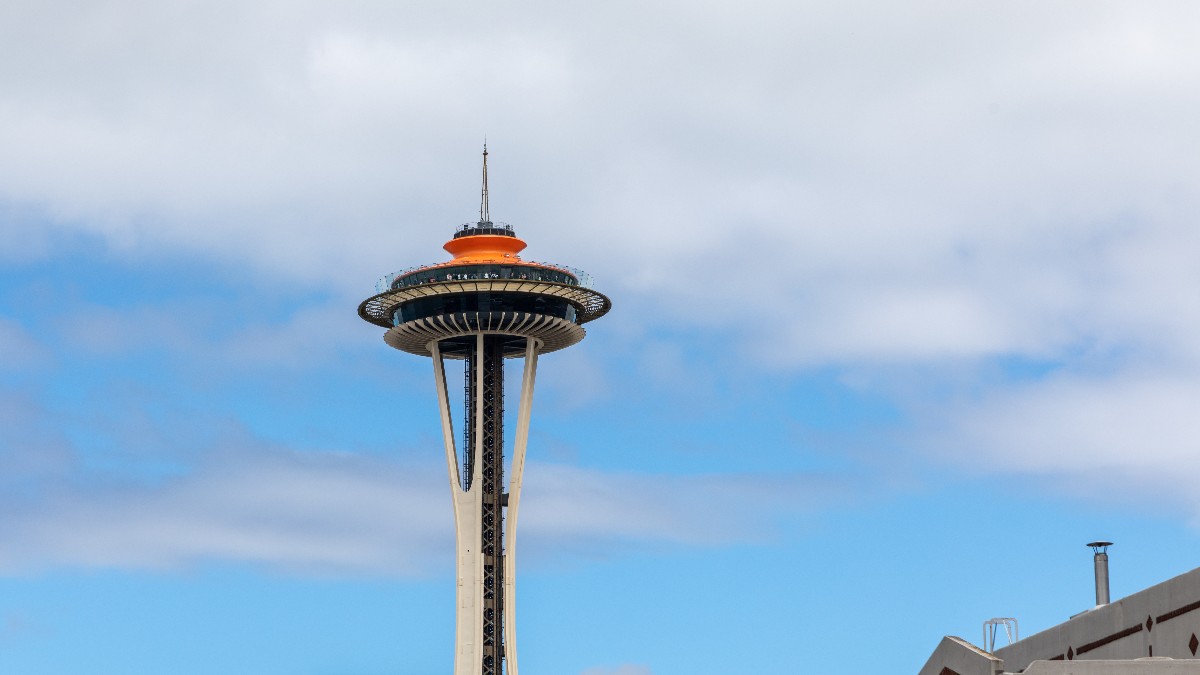 The Space Needle rises behind Seattle buildings beneath a cloudy gray sky.