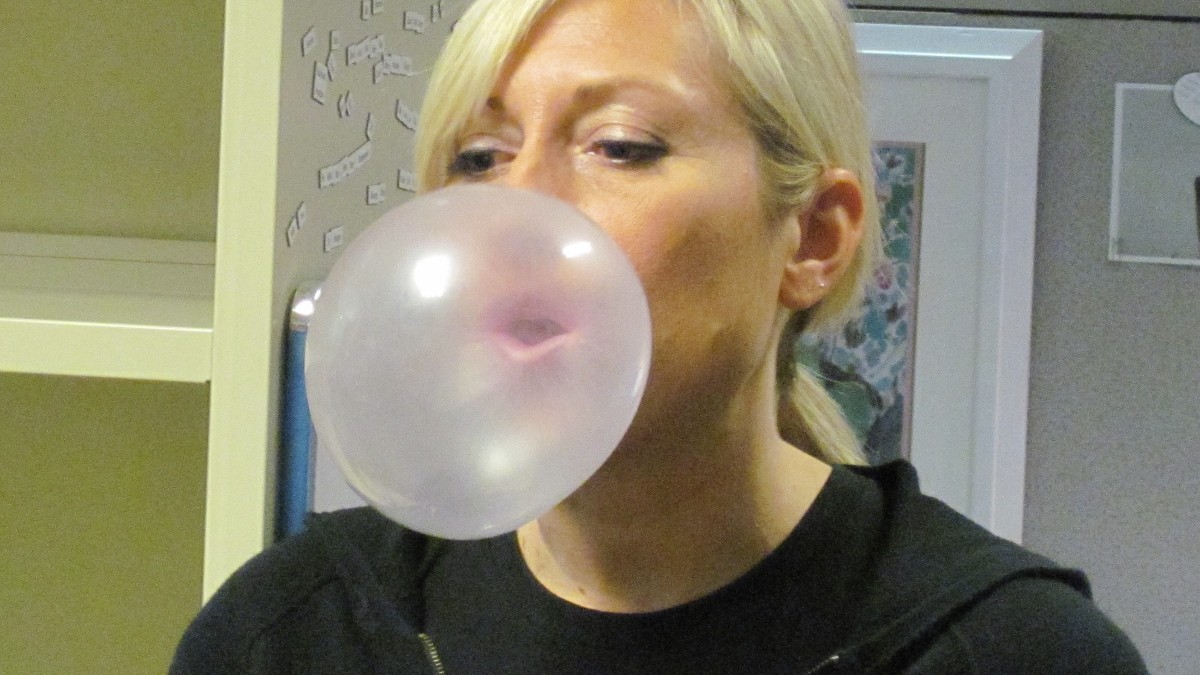 A person blowing a large pink bubble with chewing gum.