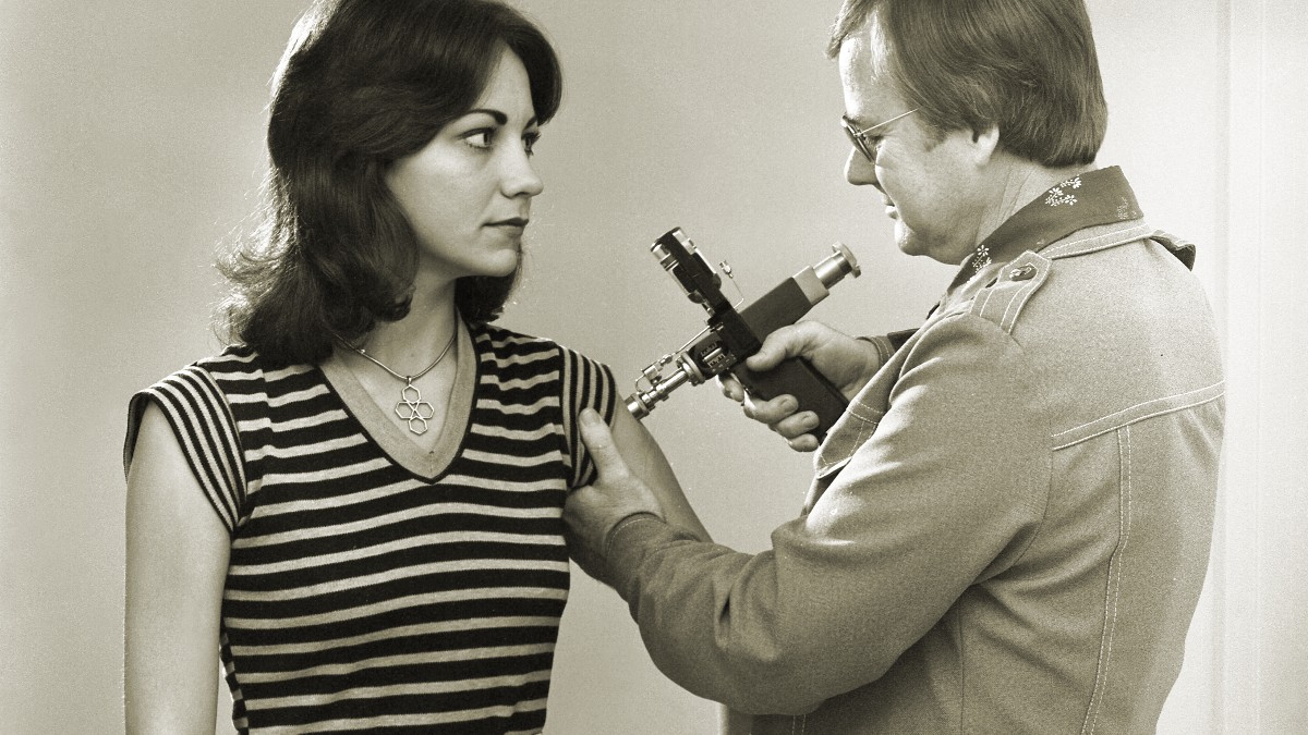 Black-and-white archival photograph of a clinician vaccinating a woman's upper arm.