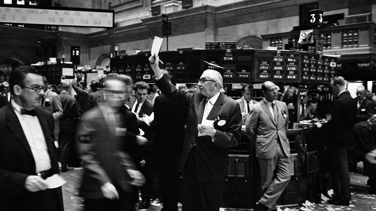Black-and-white photo of a crowded stock exchange trading floor with traders gathered around trading posts.