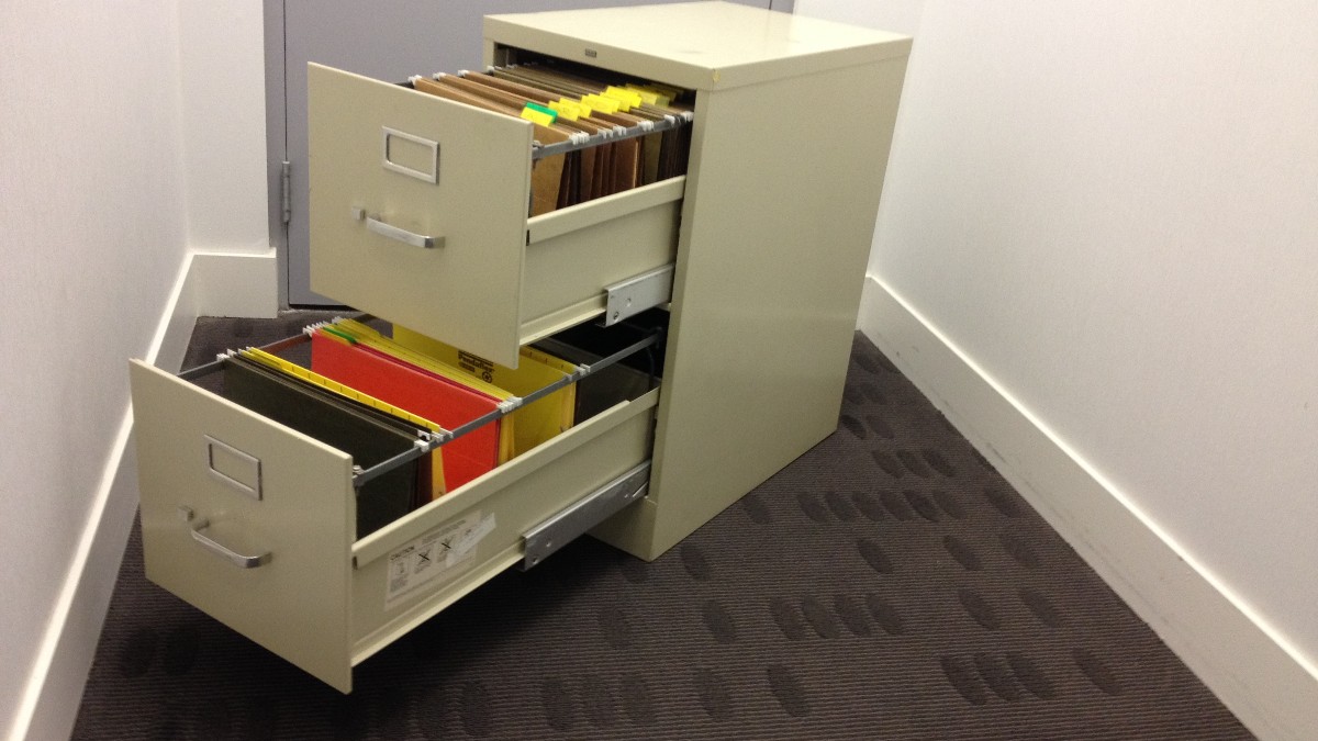 A beige two-drawer metal filing cabinet with both drawers pulled open, showing hanging folders inside, against a white wall.