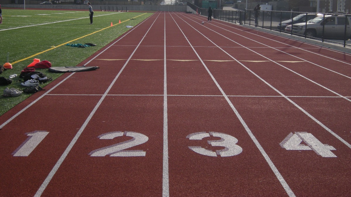 Numbered lanes 1 to 4 on a red running track at a Seattle high school, with a turf field and school buildings in the background.