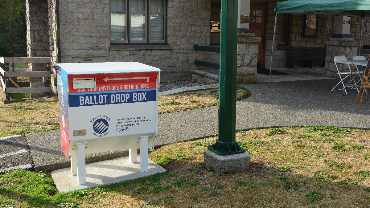 A metal ballot drop box standing on a sidewalk in front of a small town hall in Wilkeson, Washington.