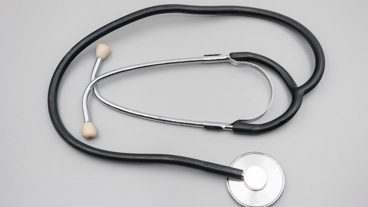 A stethoscope with black tubing and a silver chest piece lying on a plain gray surface.