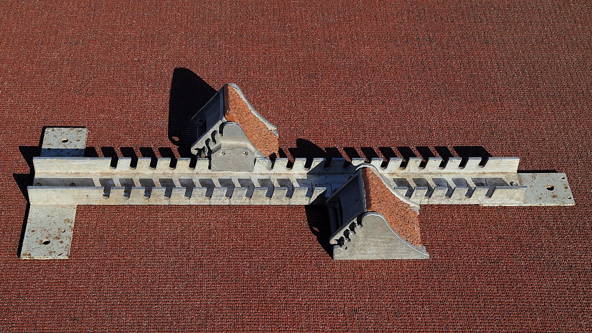 A pair of track starting blocks on a red running-track surface, seen from above.