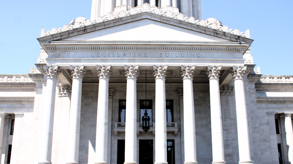 The columned front portico of the Washington State Legislative Building in Olympia, with LEGISLATIVE BUILDING carved above the columns, under a clear blue sky.