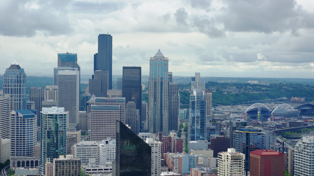 Downtown Seattle office towers seen from above under a cloudy sky, with the city's two stadiums in the background.