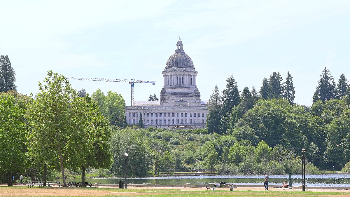 The domed Washington State Capitol seen across Capitol Lake in Olympia, with trees along the shore.